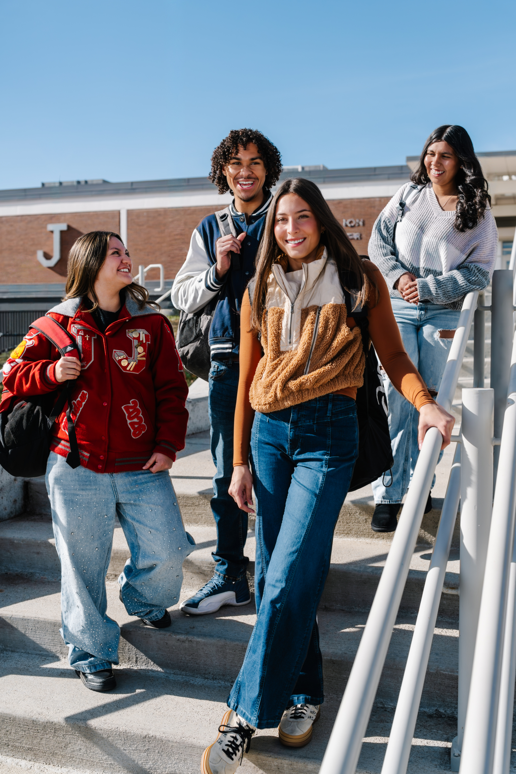 A group of teenagers stand on stairs outside of their high school